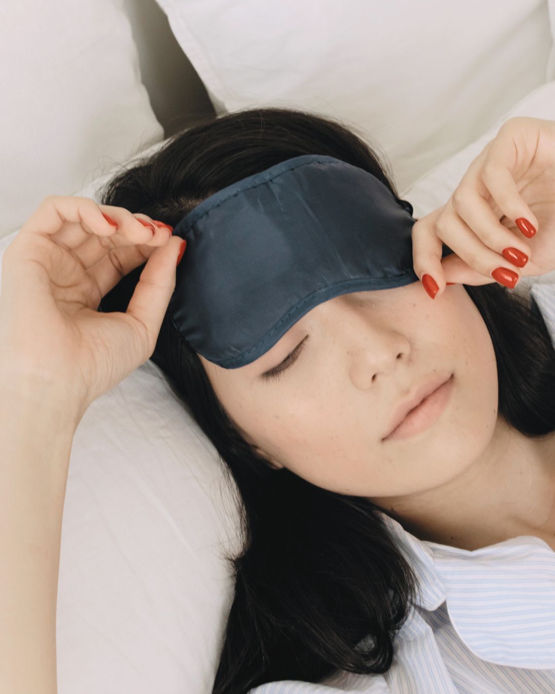 Eine Frau liegt im Bett mit einer Schlafmaske auf den Augen und ihren Fingern, die die Maske festhalten.